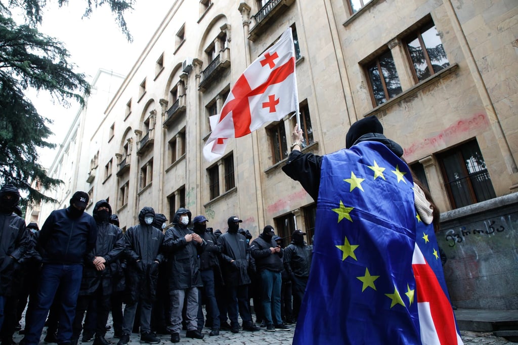 A protester waves a Georgian flag while wearing the EU flag in front of police officers blocking a street during a rally in Tbilisi, Georgia, on Tuesday. Photo: EPA-EFE A protester waves a Georgian flag while wearing the EU flag in front of police officers blocking a street during a rally in Tbilisi, Georgia, on Tuesday. Photo: EPA-EFE
