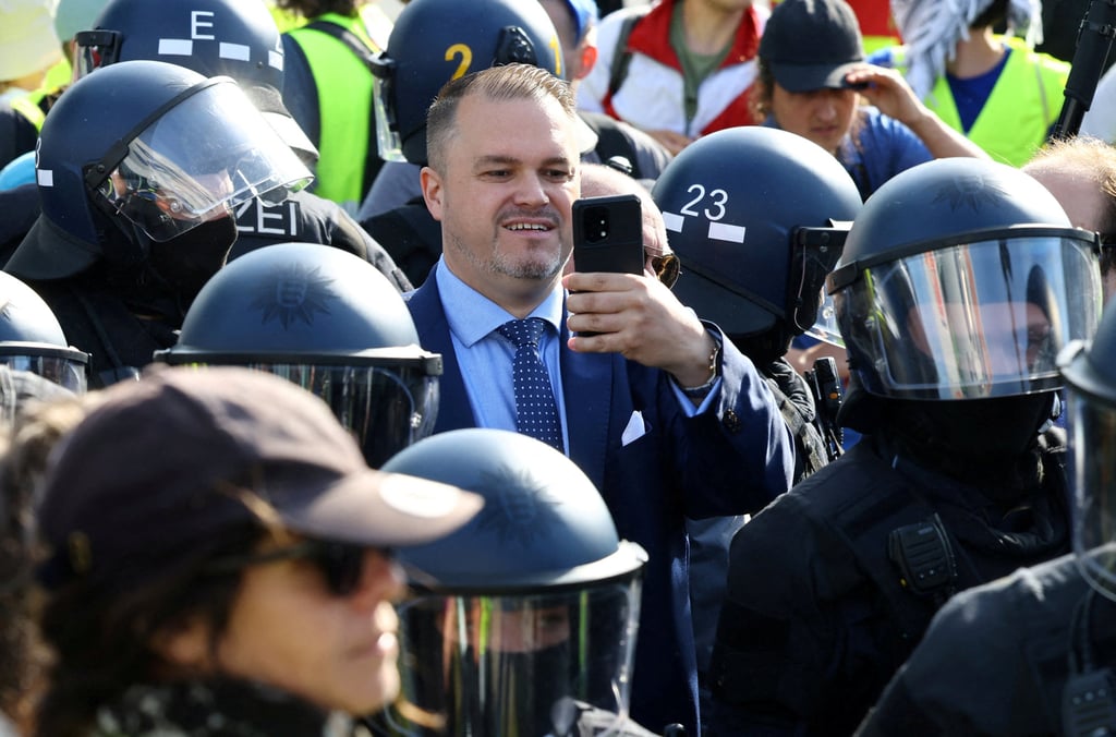 Julian Flak, member of the far-right Alternative for Germany party, uses his mobile phone while he is protected by riot police in Essen, Germany, on Saturday. Photo: Reuters Julian Flak, member of the far-right Alternative for Germany party, uses his mobile phone while he is protected by riot police in Essen, Germany, on Saturday. Photo: Reuters