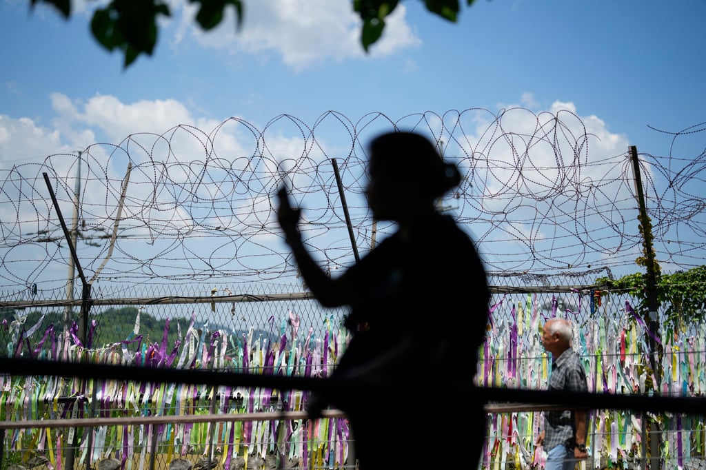 A visitor takes a photo near a wire fence decorated with ribbons written with messages wishing for the reunification of the two Koreas in Paju, South Korea, last month. Photo: AP