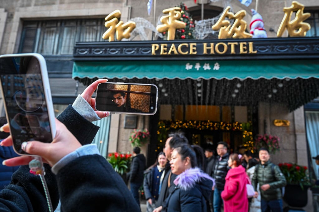 A person takes a photo of The Fairmont Peace Hotel in Shanghai – formerly the Cathay Hotel featured in Blossoms Shanghai – together with a phone image of Hu Ge, who plays Ah Bao in the series. Photo: AFP