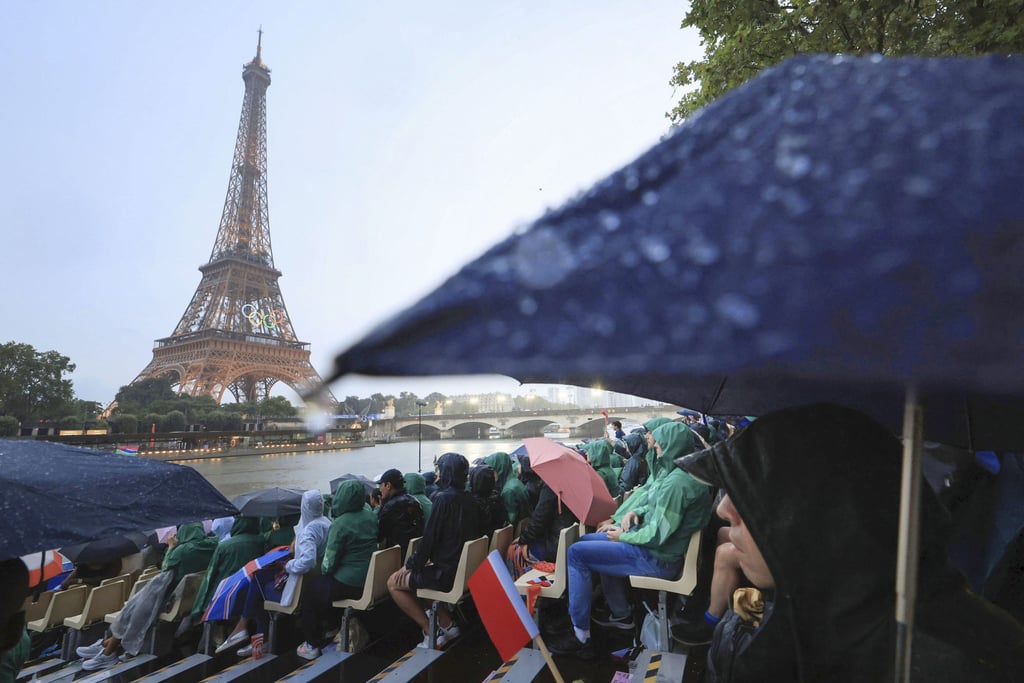 Spectators shield themselves from the rain during the Paris Olympics opening ceremony. Photo: Kyodo