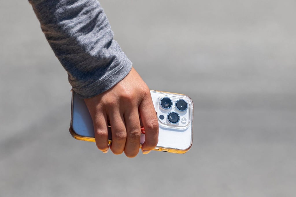 A pedestrian holds an iPhone in front of an Apple store in San Francisco, California, June 11, 2024. Photo: Bloomberg