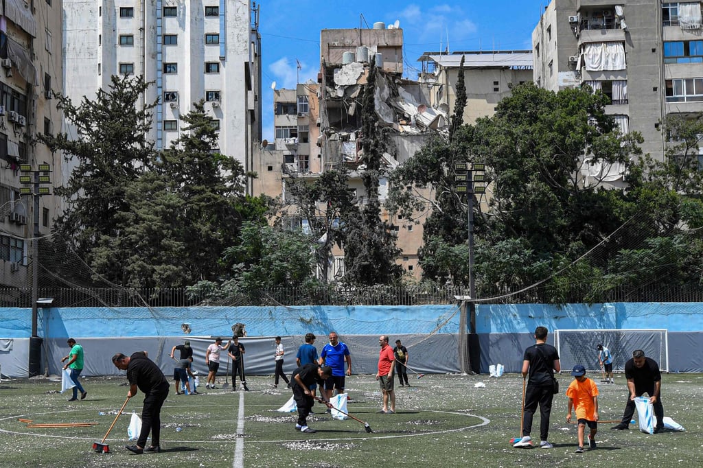 Residents on Wednesday clear the rubble in a football field facing the building that was hit a day earlier in an Israeli strike in Beirut’s southern suburbs. Photo: AFP