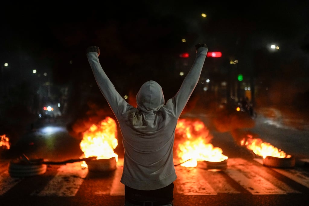 A protester raises his arms in front of burning tyres in Caracas on Monday. Photo: AP Maduro pide al Tribunal Supremo de Justicia que audite las elecciones en disputa