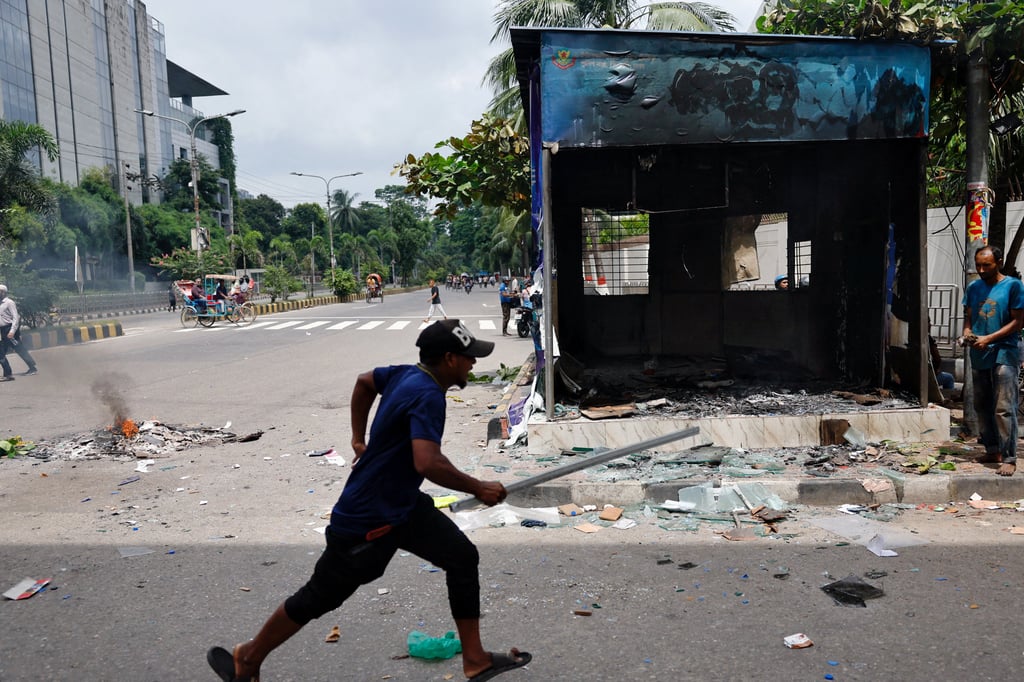 A demonstrator runs next to a vandalised police box in Dhaka, Bangladesh. Photo: Reuters