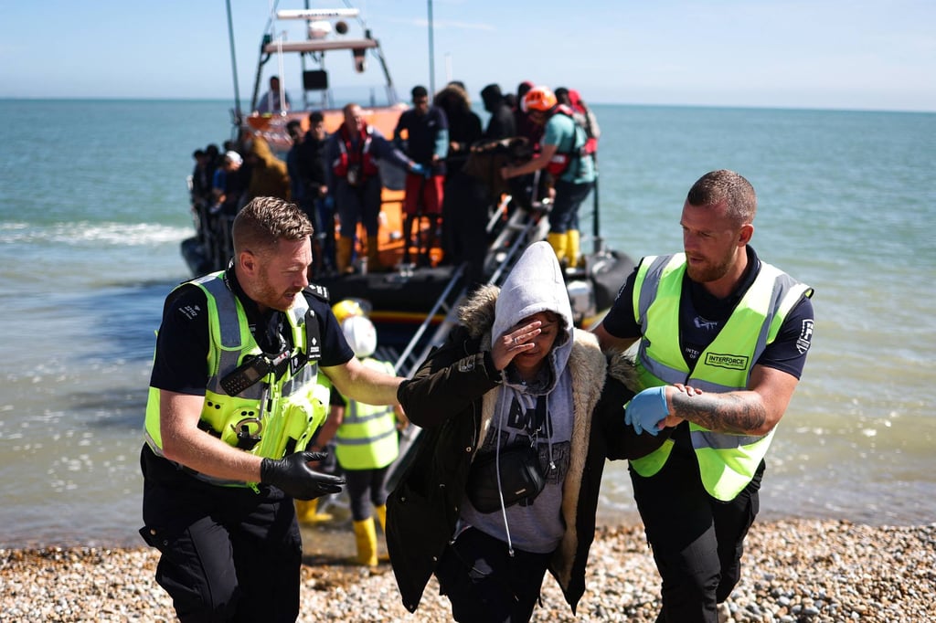 Un agente interfuerzas y un agente de la fuerza fronteriza ayudan a una mujer en la playa de Dungeness, en el sureste de Inglaterra, después de que un bote salvavidas de la Royal National Lifeboat Institution (RNLI) la recogiera en el mar junto con otros inmigrantes mientras intentaban cruzar el Canal de la Mancha desde Francia en agosto del año pasado. Foto: AFP