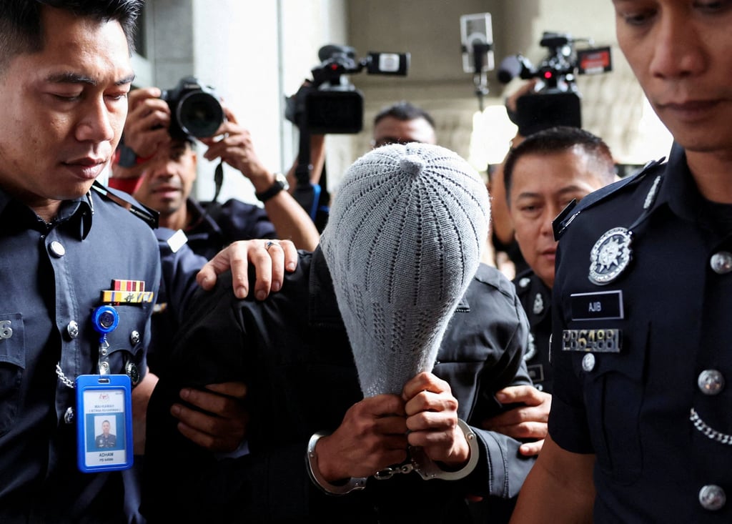 A man linked to Global Ikhwan Service and Business Holdings (GISB) covers his face as he is escorted by police officers after being charged in a court in Putrajaya on September 18. Photo: Reuters