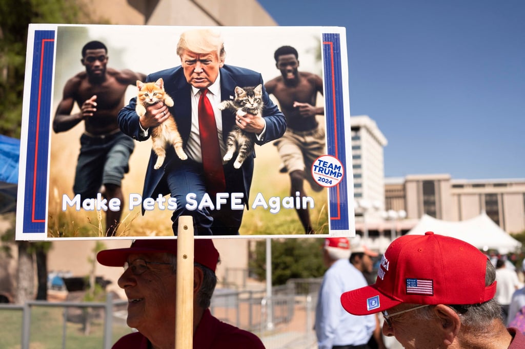 A man carries an AI-generated image of Donald Trump carrying cats away from Haitian immigrants, during a campaign rally for Trump in Tucson, Arizona. Photo: TNS