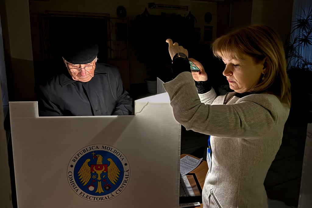An election official assists a voter with her mobile phone flashlight during a power failure in Chisinau, Moldova. Photo: AP