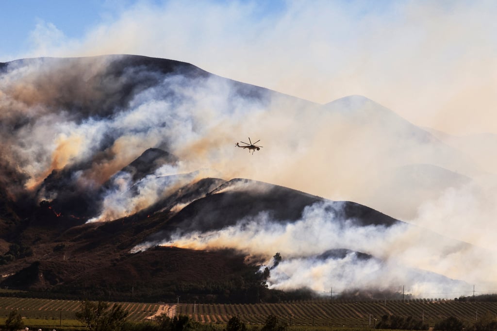 An helicopter flies as smoke billows from the Mountain Fire in Santa Paula, California. Photo: Reuters