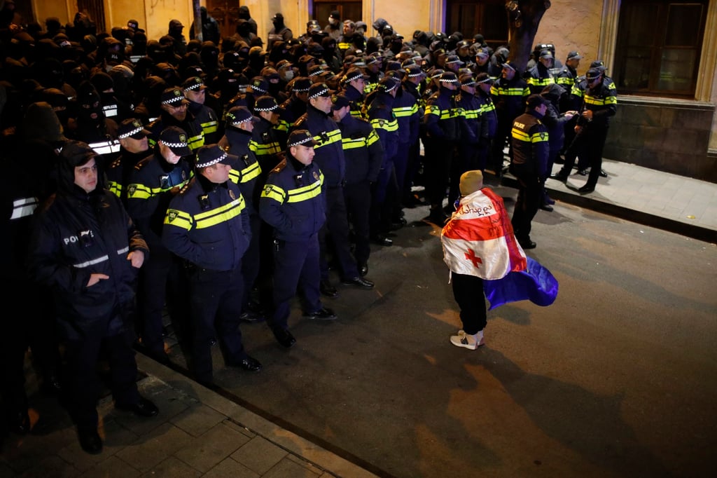 A protester wearing Georgian and EU flags faces police officers during a rally in Tbilisi on Sunday. Photo: EPA-EFE