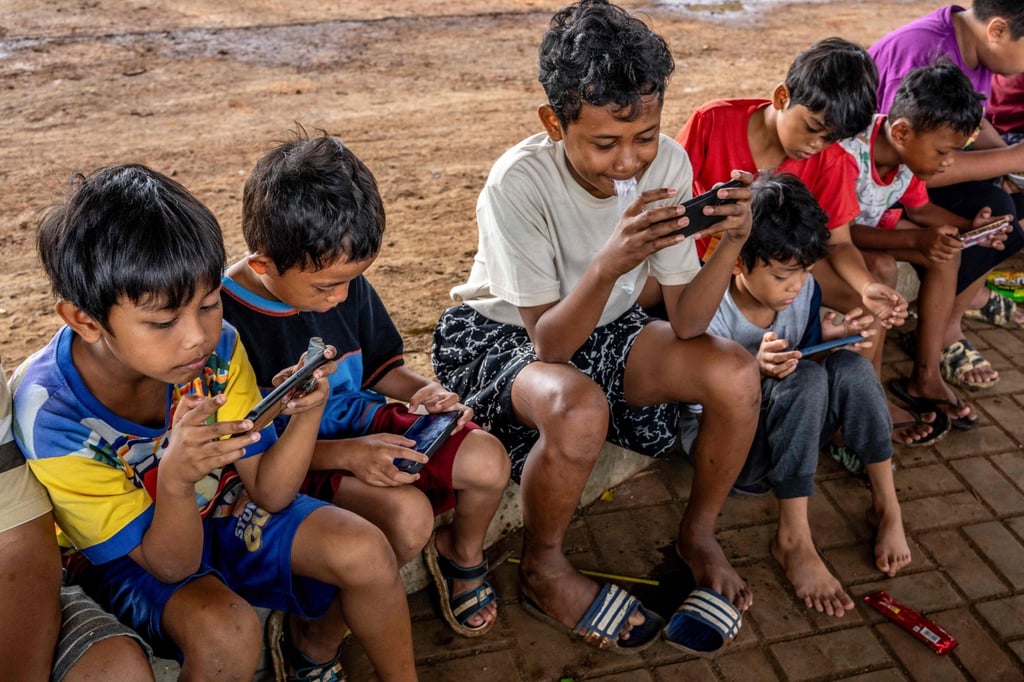 Children look at their mobile phones along a roadside in Jakarta on Wednesday. Photo: AFP Children look at their mobile phones along a roadside in Jakarta on Wednesday. Photo: AFP