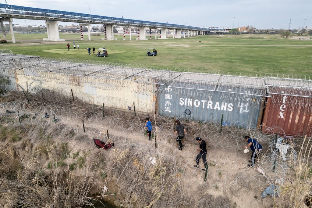 Migrants walk on the banks of the Rio Grande river to find a way to enter the US as golfers play on the other side of the shipping container fence in Eagle Pass, Texas. Photo: Reuters