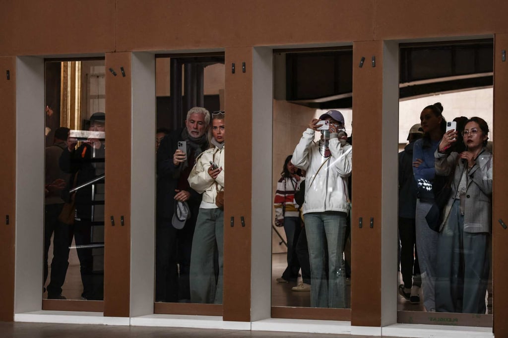 Visitors watch through glass panes as art restorers work on Gustave Courbet’s painting A Burial at Ornans at the Orsay Museum. Photo: AFP