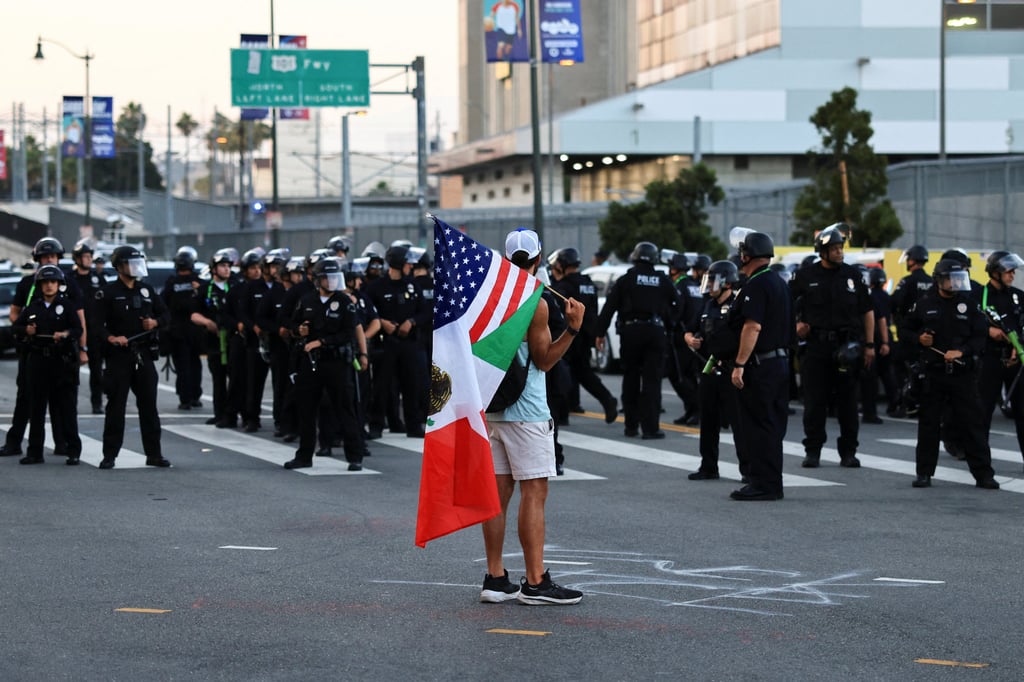 A person holds a mixed Mexico–US flag as law enforcement officers stand guard in Los Angeles. Photo: Reuters