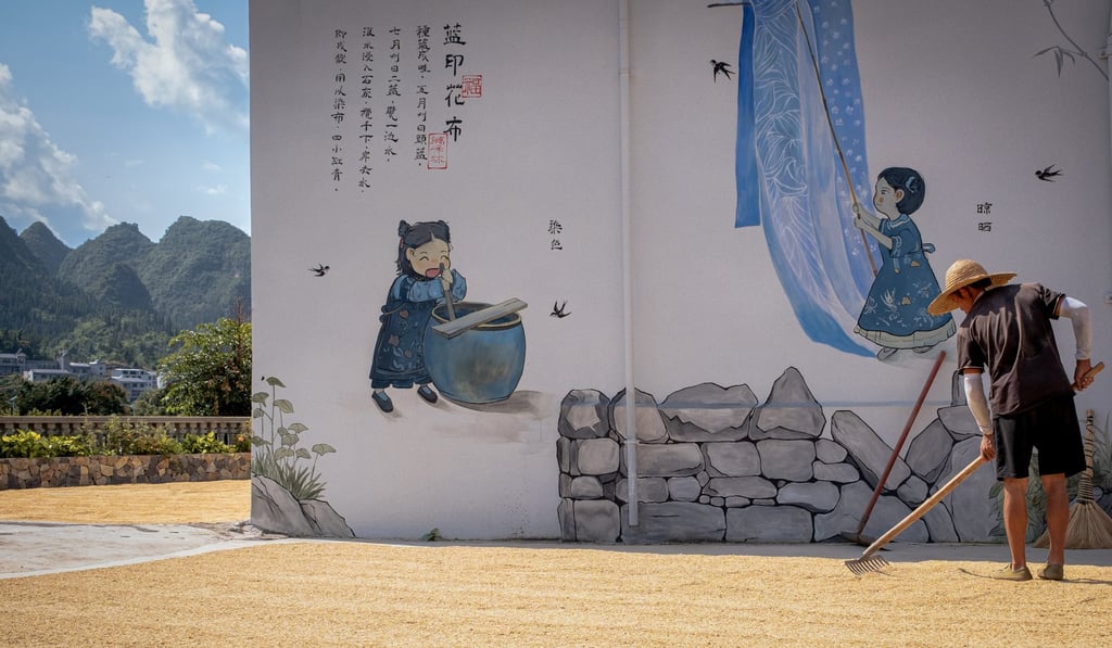 A farmer in Wanfu village rakes maize in front of a mural-covered home. Photo: Chan Kit Yeng