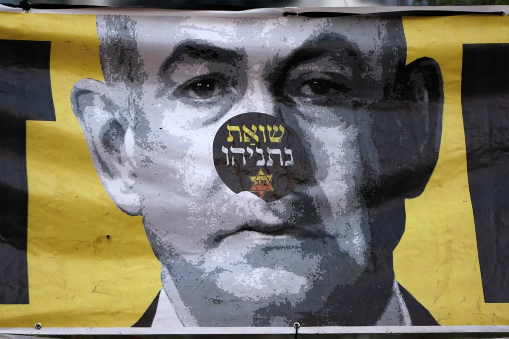A sticker reading “Netanyahu’s Holocaust” in Hebrew is displayed above a banner depicting the Israeli prime minister during an anti-government protest in Tel Aviv on Saturday. Photo: AFP A sticker reading “Netanyahu’s Holocaust” in Hebrew is displayed above a banner depicting the Israeli prime minister during an anti-government protest in Tel Aviv on Saturday. Photo: AFP