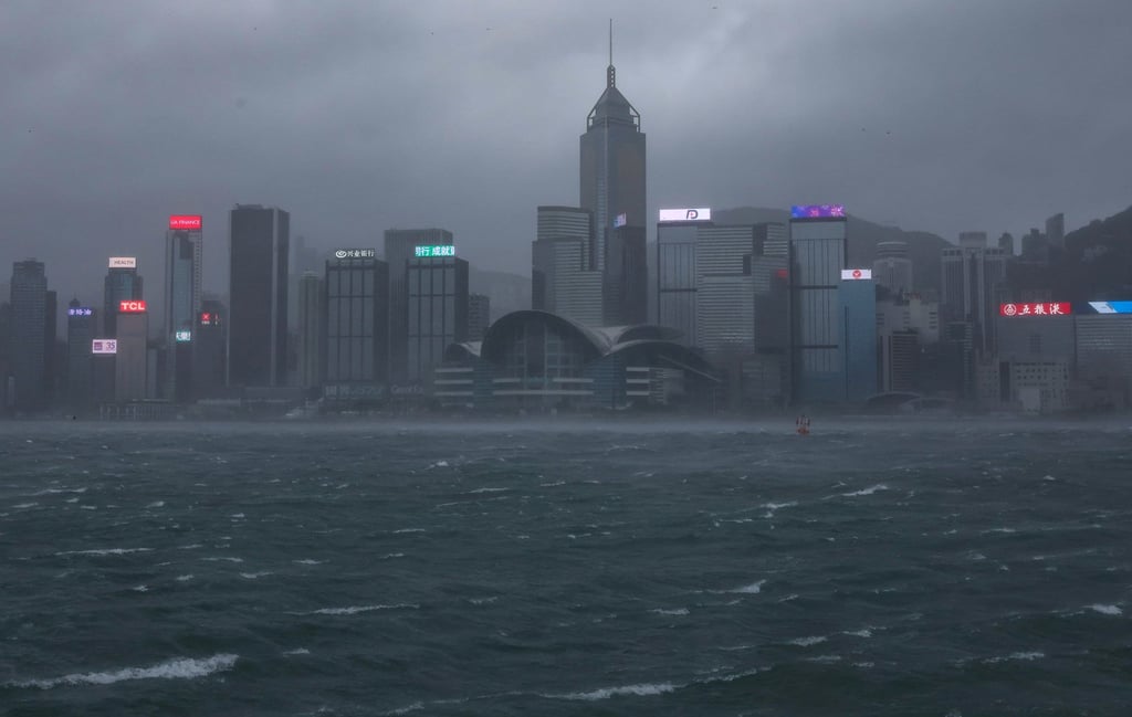 Hong Kong's skyline is shrouded in fog and heavy rain as Tropical Storm Tapah approaches, with rough seas and dark, stormy clouds overhead.