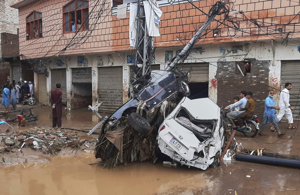 Residents walk next to damaged cars stuck to an electric pole following flash floods in Mingora, northwestern Pakistan, on Friday. Photo: AP Residents walk next to damaged cars stuck to an electric pole following flash floods in Mingora, northwestern Pakistan, on Friday. Photo: AP