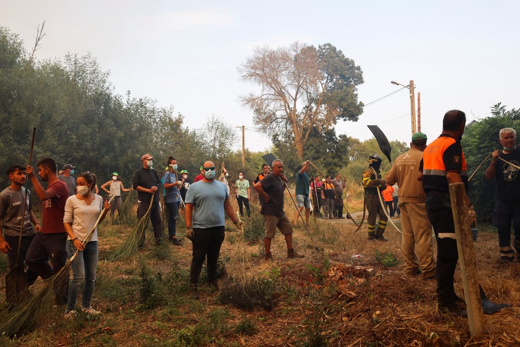 Residents hold fire beaters and tree branches as they gather to help extinguish a wildfire in Veiga das Meas, near Verin, Ourense province, in Galicia, Spain, on Saturday. Photo: Reuters