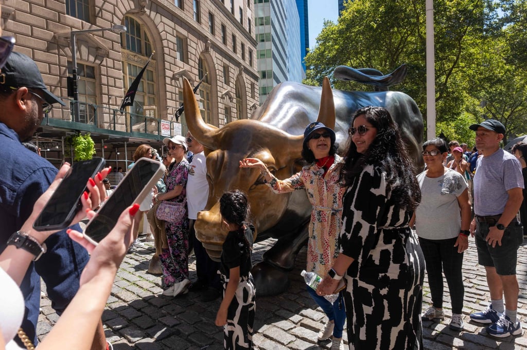 People gather near the Wall Street bull near the New York Stock Exchange. US stocks rose sharply on Friday after Federal Reserve chair Jerome Powell hinted at a near-term interest-rate cut. Photo: Getty Images via AFP People gather near the Wall Street bull near the New York Stock Exchange. US stocks rose sharply on Friday after Federal Reserve chair Jerome Powell hinted at a near-term interest-rate cut. Photo: Getty Images via AFP