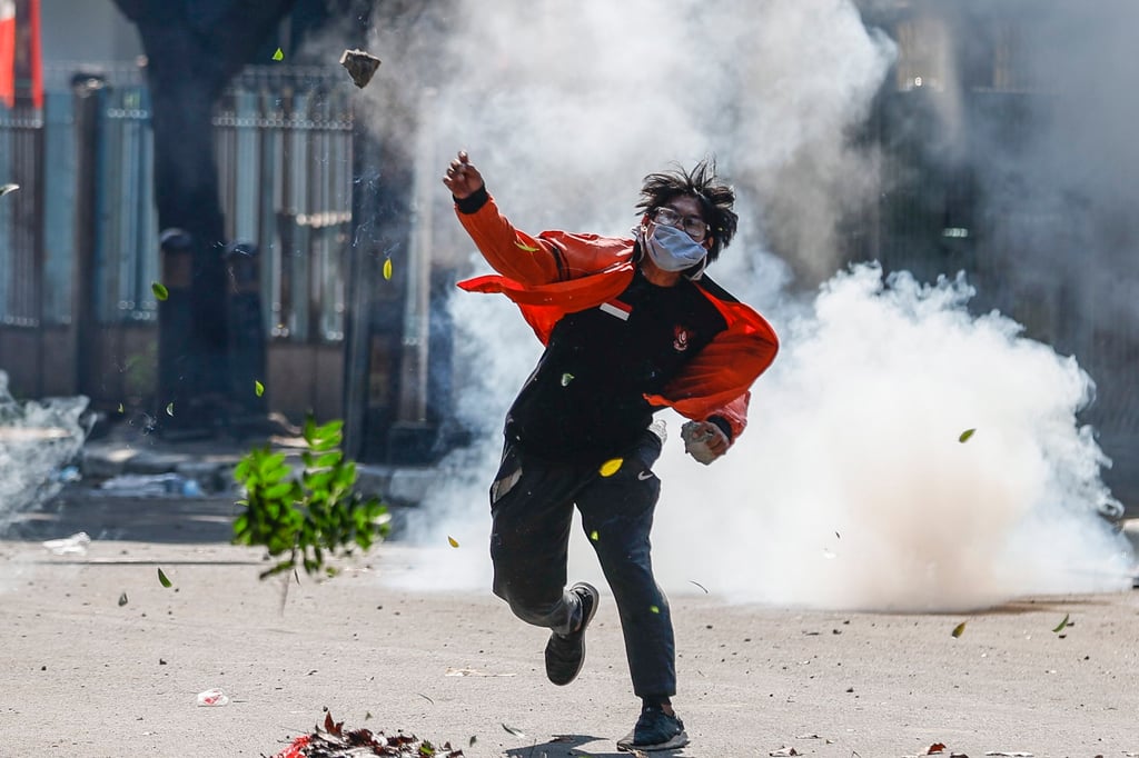 A protester throws a rock as a tear-gas canister explodes during clashes with police in Jakarta. Photo: EPA A protester throws a rock as a tear-gas canister explodes during clashes with police in Jakarta. Photo: EPA