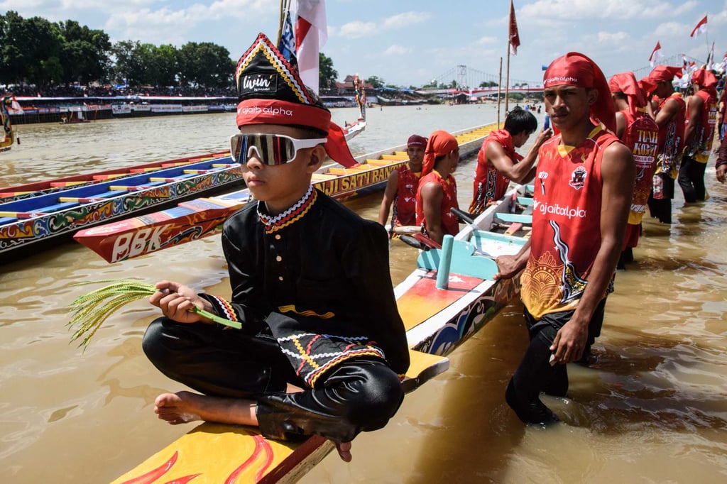 Rayyan Arkan Dikha (left), sits on his team’s vessel before competition during the Pacu Jalur longboat race festival on the Kuantan River in Kuantan Singingi Regency, Riau Province, on August 22. Photo: AFP