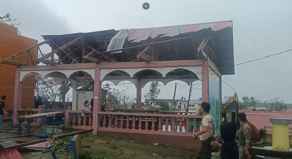 People walk past a building with ripped-off roof near a church in Bicol’s Masbate City on Friday. Photo: Engineer Jerome Martinez/AFP