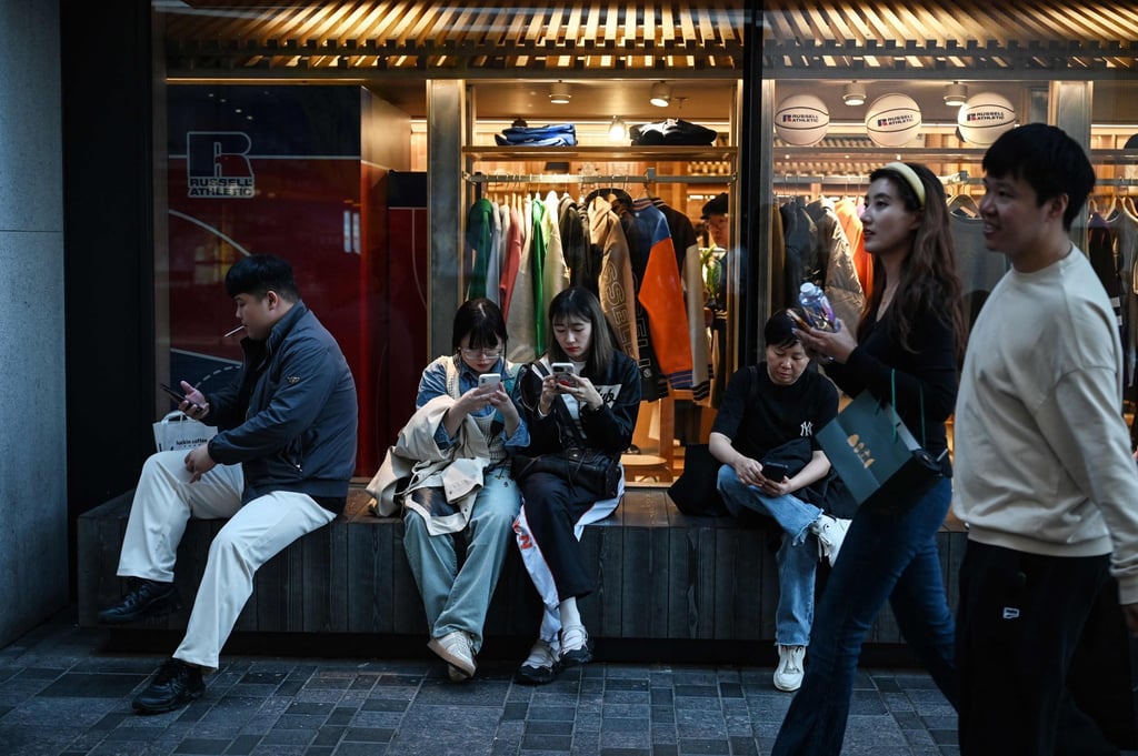 People use their smartphones outside a clothing store in Beijing on October 4, 2024. Photo: AFP People use their smartphones outside a clothing store in Beijing on October 4, 2024. Photo: AFP
