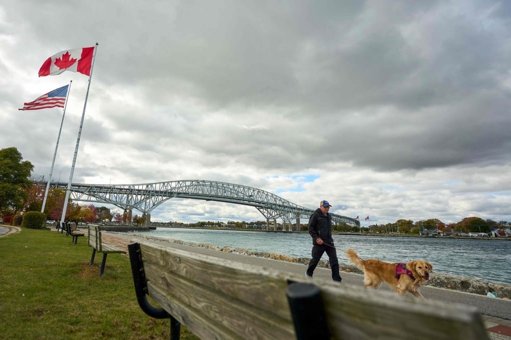 US and Canadian flags fly as a man walks his dog along the St Clair River backdropped by the Blue Water Bridge border crossing in Point Edward, Ontario, on October 24. Photo: AFP