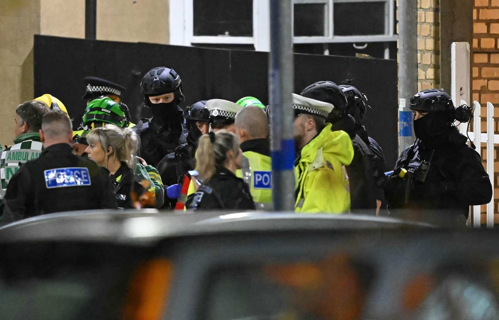 Armed police officers stand with members of the emergency services outside Huntingdon Station in eastern England on Saturday. Photo: AFP