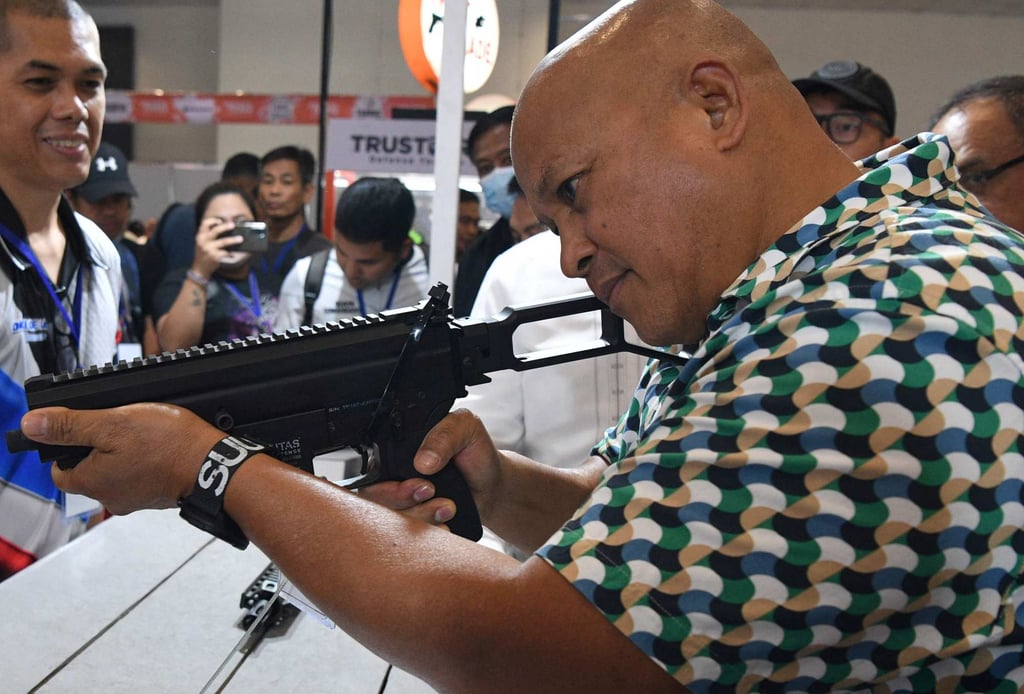 Senator Ronald Dela Rosa tries a semi-automatic rifle during a defence and sporting show in May 2023. Photo: AFP