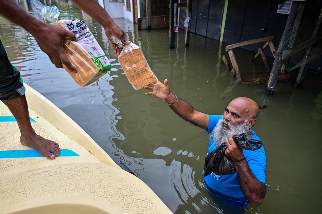 A man distributes bread to flood victims on the outskirts of Colombo on Saturday. At least 123 people have died after a cyclone hit their country. Photo: AFP