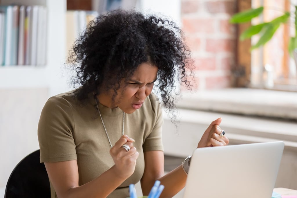 A woman angrily gestures at her laptop, highlighting the negativity of social media, where “rage bait” has become widespread. Photo: Shutterstock