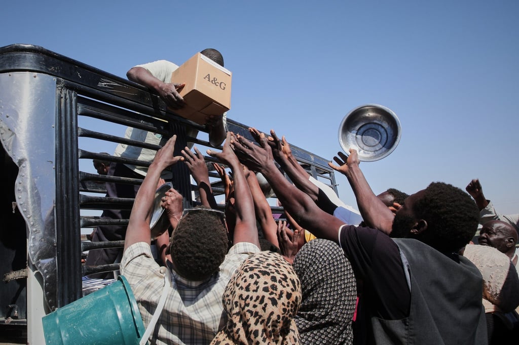 Sudanese families displaced from El-Fasher reach out as aid workers distribute food at El-Afadh camp in Al Dabbah in November. Photo: AP
