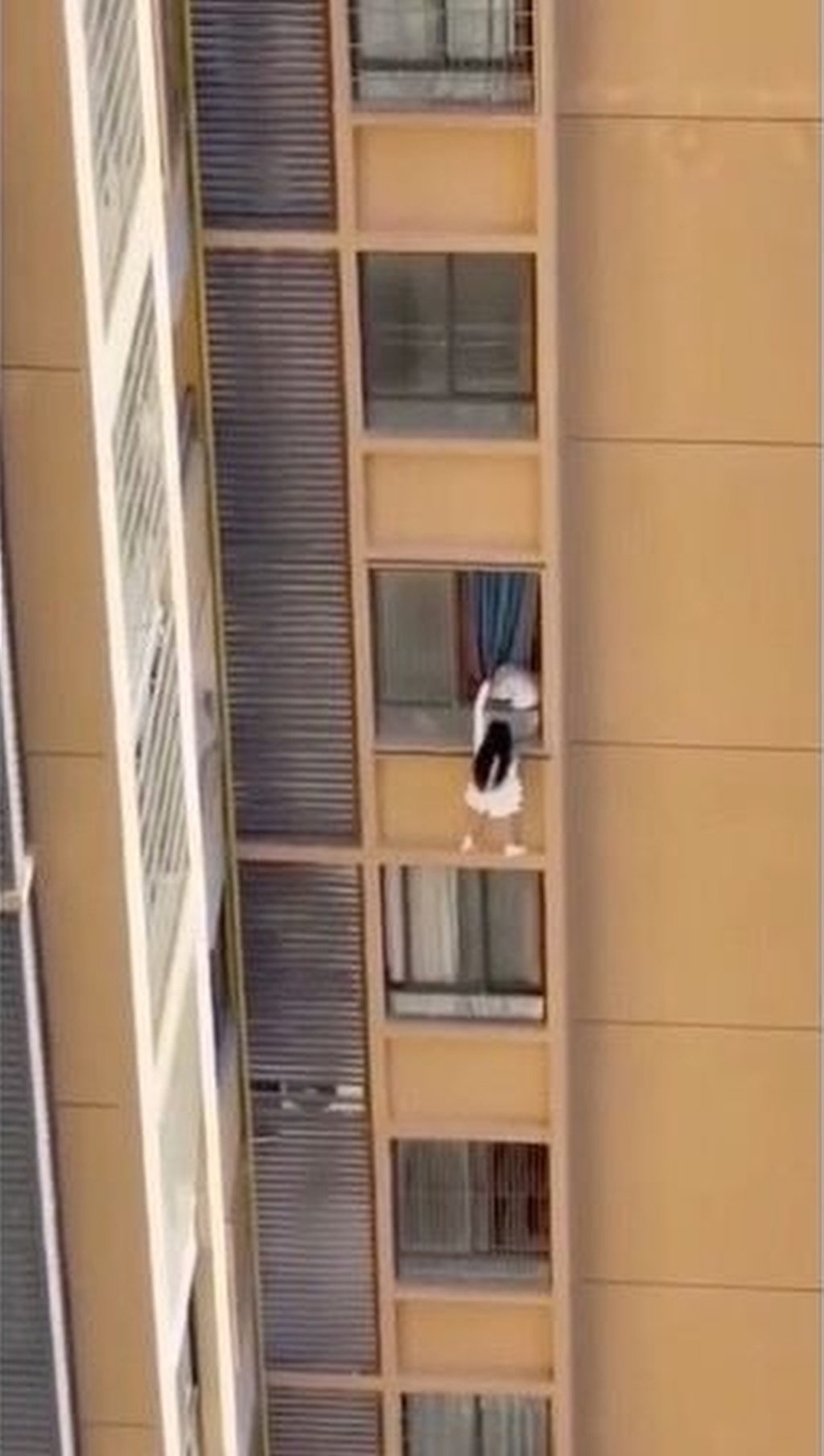 The woman is seen perched on a wall high up on the building while holding onto a curtain. Photo: ettoday.net The woman is seen perched on a wall high up on the building while holding onto a curtain. Photo: ettoday.net