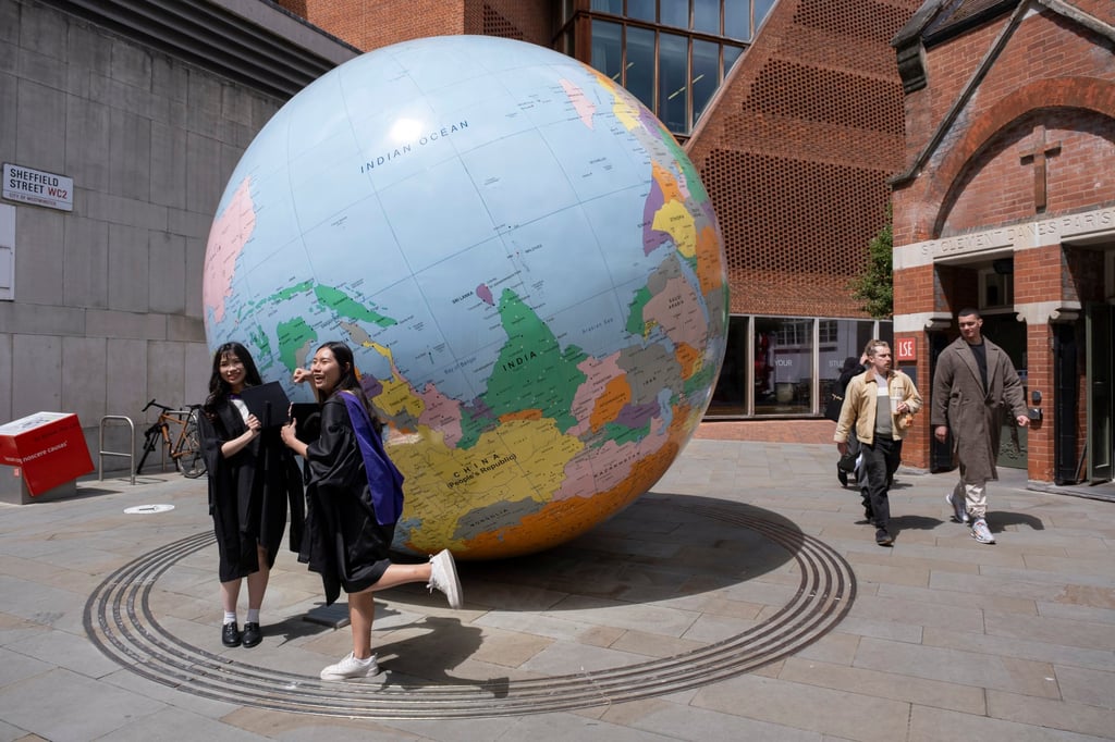 Students in graduation gowns pose by The World Turned Upside Down sculpture at the London School of Economics on June 10, 2024, in London, England. Photo: In Pictures via Getty Images