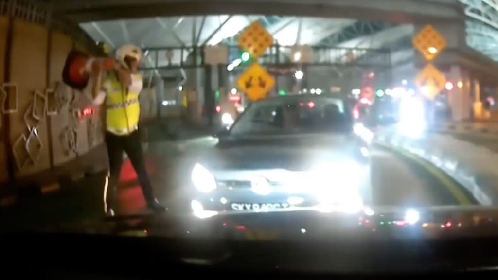 A Malaysian officer tries to hit the Singapore-registered car’s bonnet with a traffic cone to prevent the driver from fleeing. Photo: Handout