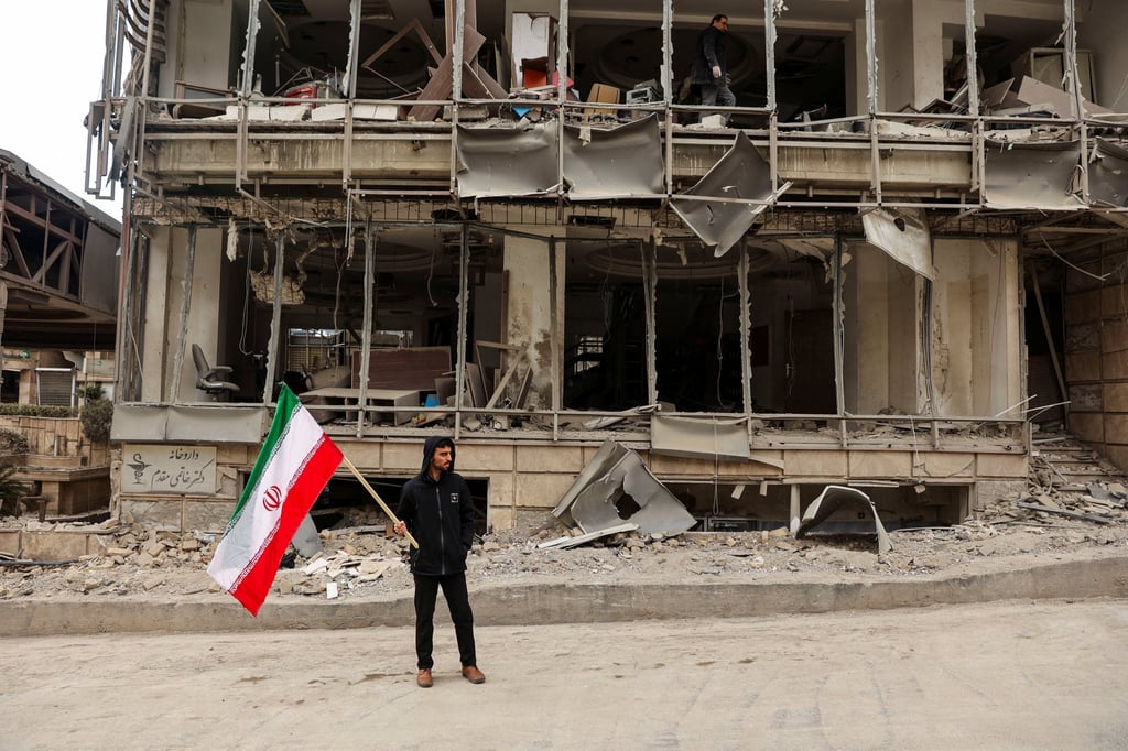 A man holds an Iranian flag following an Israeli and US strike on Gandhi Hotel Hospital in Tehran on Monday. Photo: West Asia News Agency via Reuters