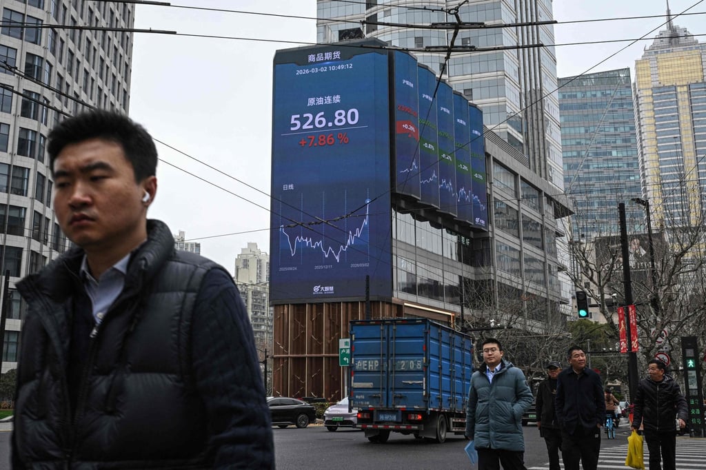 Pedestrians walk next to a screen showing commodity futures for crude oil in Shanghai on Monday. Photo: AFP