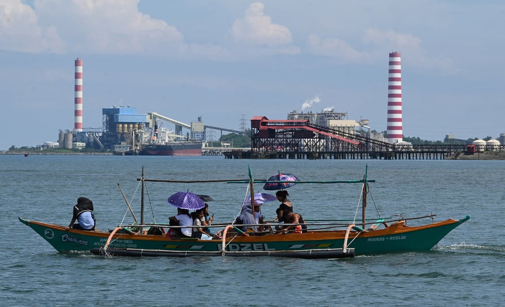 People sail past a coal-fired power plant in Oyon Bay in the Philippines. Photo: AFP
