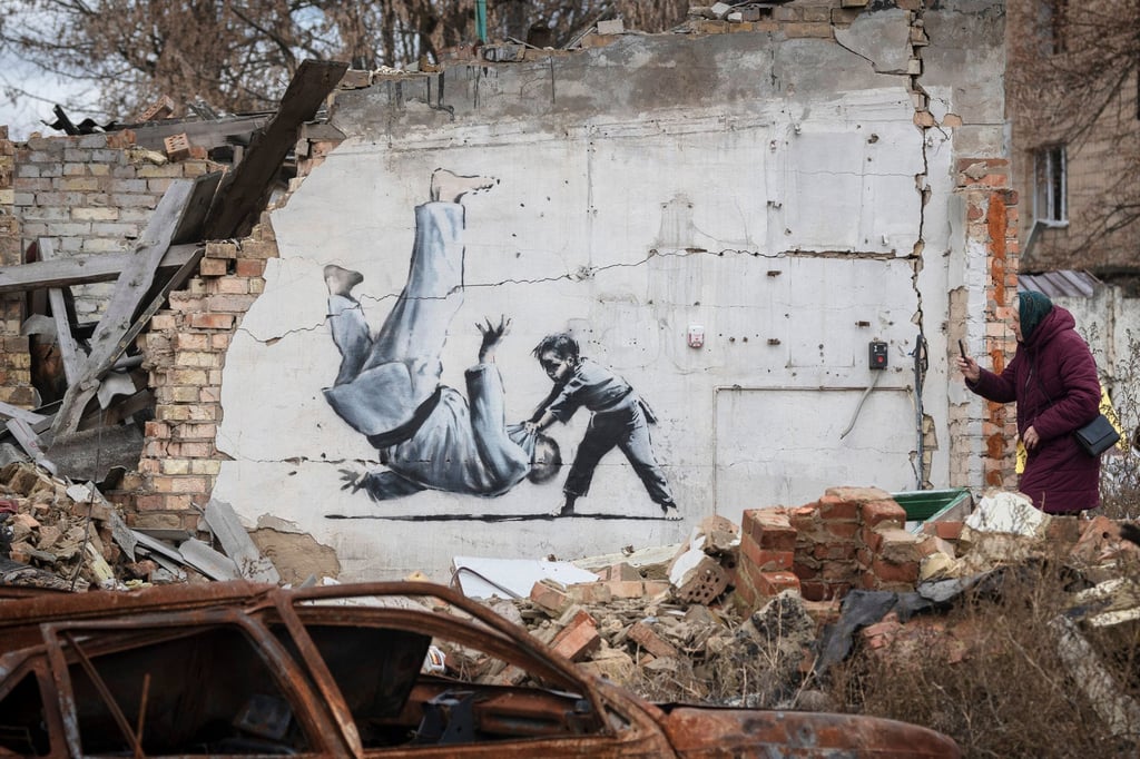 A woman takes a picture of a suspected Banksy piece on a destroyed building in the Ukrainian town of Borodyanka, in November 2022. Photo: AP