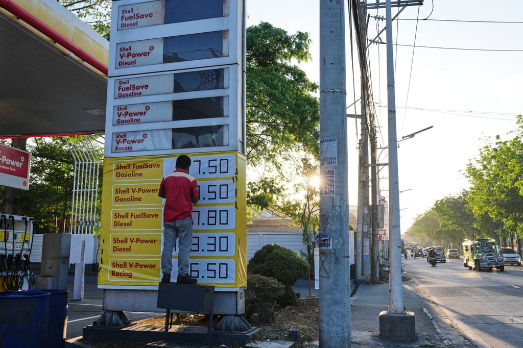 A worker uses black tape to adjust the prices on a digital sign board that cannot accommodate additional digits at a petrol in Quezon City, Philippines, on Tuesday. Photo: AP A worker uses black tape to adjust the prices on a digital sign board that cannot accommodate additional digits at a petrol in Quezon City, Philippines, on Tuesday. Photo: AP