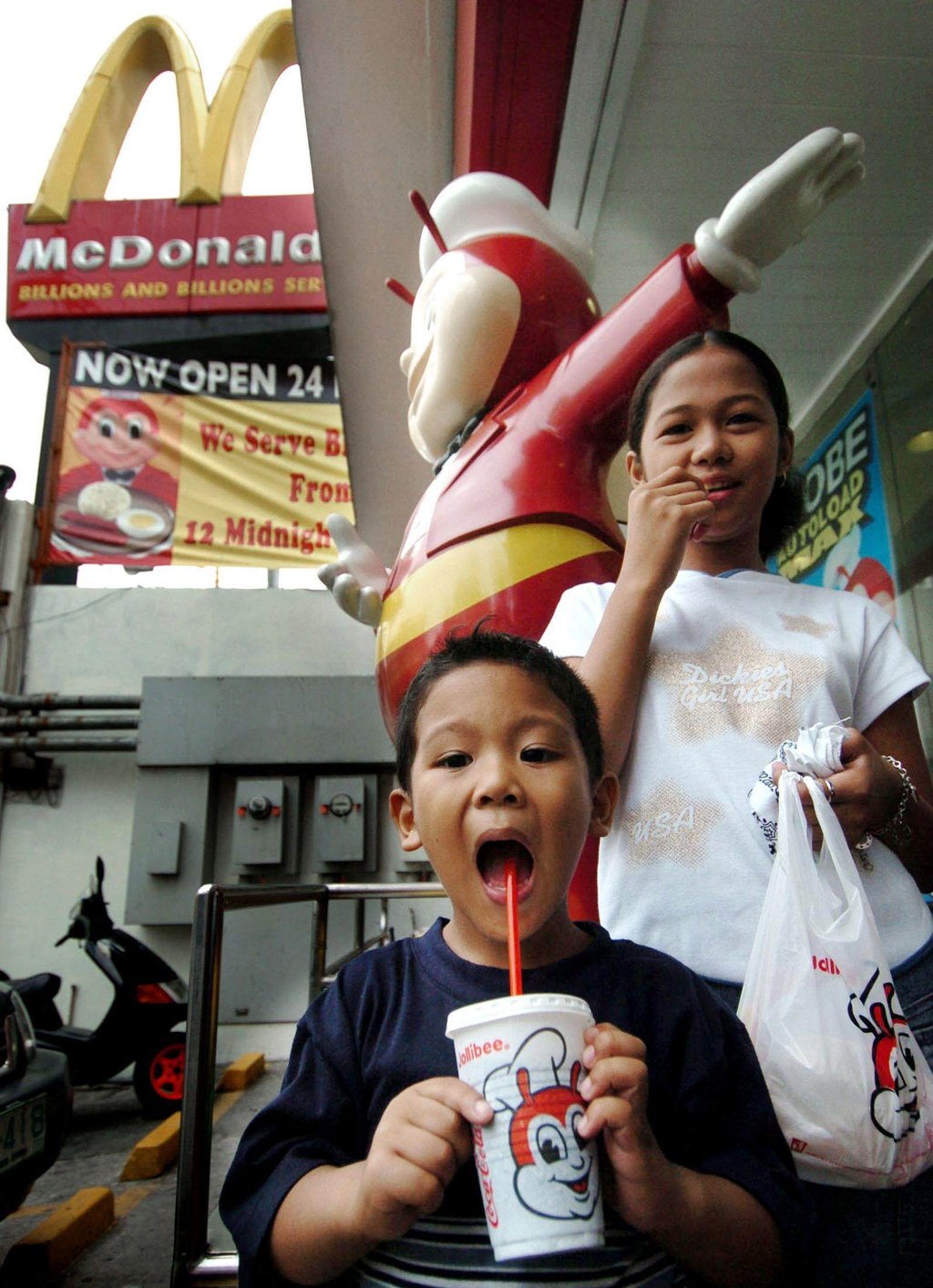 Children enjoy Jollibee snacks outside an outlet in Manila with a McDonald's logo in the background. Photo: AFP
