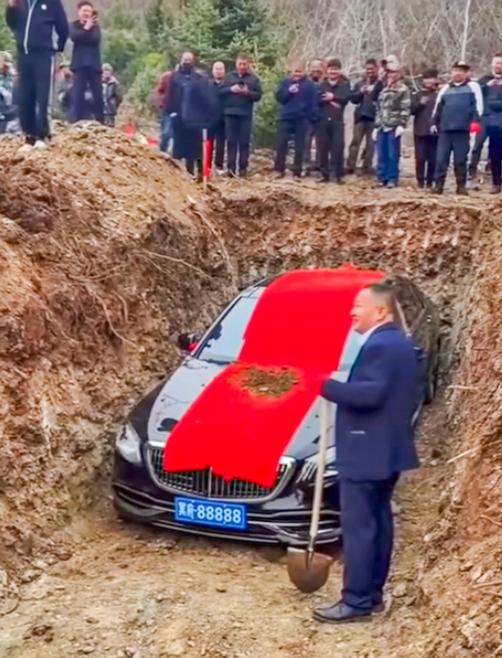 A mourner stands next to the about to be buried luxury car holding a spade. Photo: bilibili.com