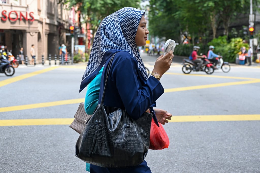 A woman uses a portable fan in Kuala Lumpur. Malaysian authorities warn that prolonged strenuous physical activity could lead to dehydration. Photo: AFP