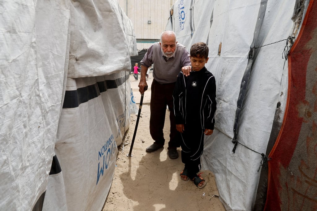 Displaced Palestinian Mustafa Al-Jazzar, 83, who fled his hometown in 1948, walks with the help of a boy at a camp for displaced people in the southern Gaza Strip on Tuesday. Photo: Reuters
