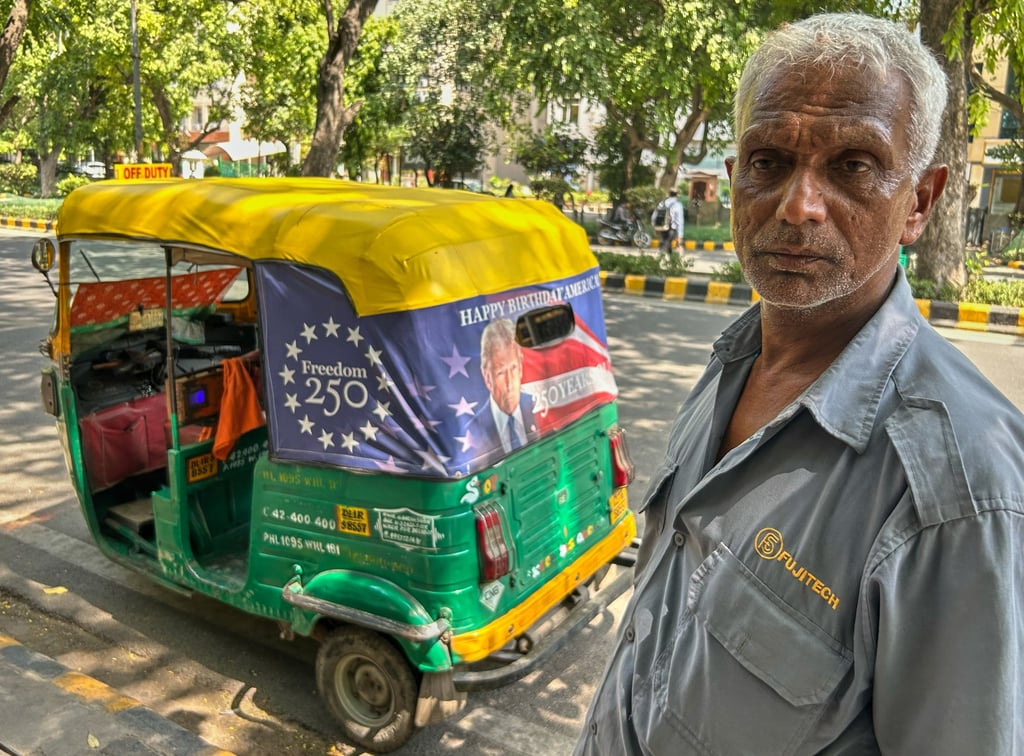 Ganesh Kumar stands with a poster of US President Donald Trump that he agreed to put up on his autorickshaw for a packet of tea on Wednesday. Photo: AP