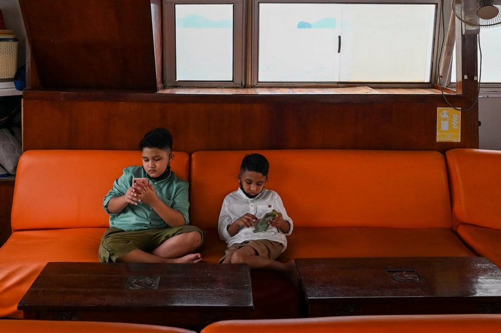 Two boys play with their mobile phones on board a catamaran yacht in Langkawi, Malaysia. Photo: AFP