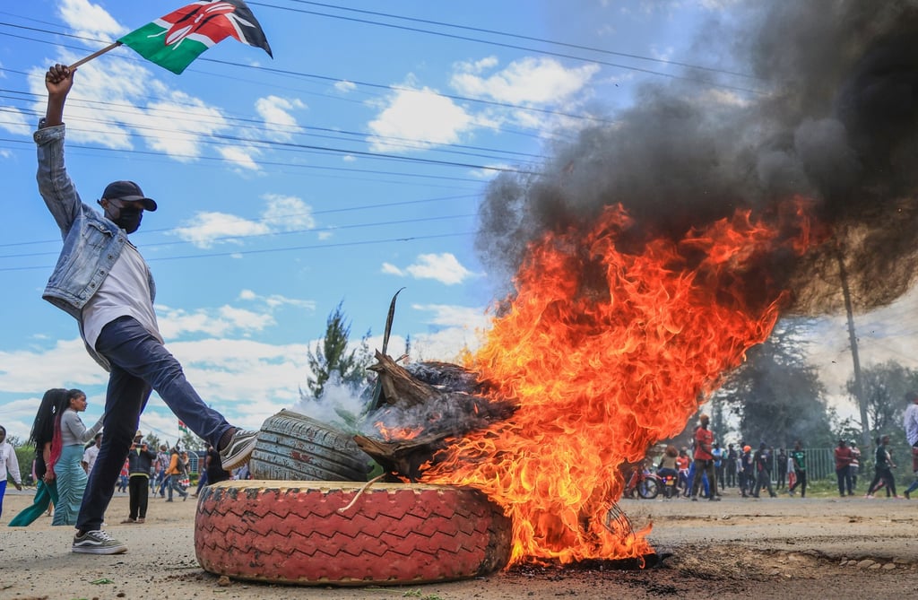 A protester raises a Kenyan flag near a burning barricade during a protest against a proposed Ebola quarantine centre to be established by the US in Nanyuki, Kenya. Photo: AP A protester raises a Kenyan flag near a burning barricade during a protest against a proposed Ebola quarantine centre to be established by the US in Nanyuki, Kenya. Photo: AP